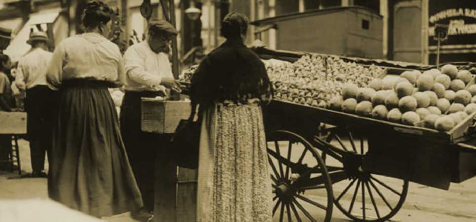 A woman selling fresh fruit on a bustling street in the early 1900s